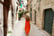 Woman with long orange summer dress walking in narrow alley of Bisceglie medieval historical town of Apulia, Italy