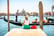 Young female traveler sitting on the pier and enjoying beautiful view on venetian chanal with gondolas floating in Venice