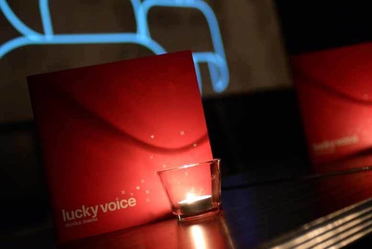 A Lucky Voice drinks menu next tot a candle