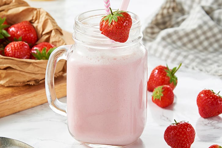 A strawberry milkshake in a mason glass jar with actual strawberries surrounding it