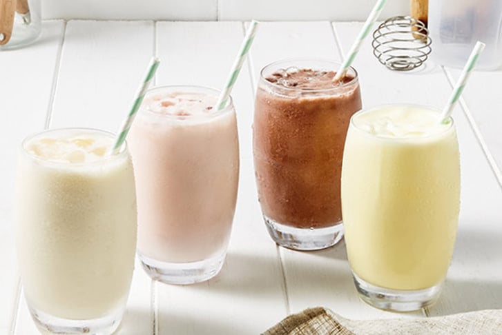 Four milksakes (banana, strawberry, chocolate and vanilla) on a table with straws in them