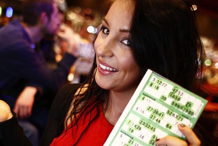 A woman holding up her bingo card, despite the fact she is still two numbers off a full house 