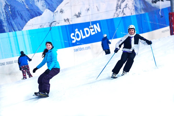 Two people skiing and snowboarding down a slope
