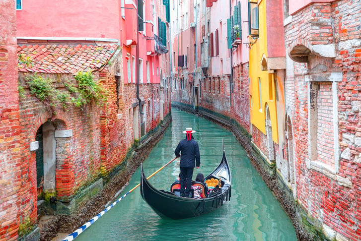 Venetian gondolier punting gondola through green canal waters of Venice Italy