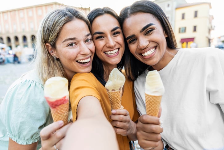 Happy women eating ice cream walking on city street