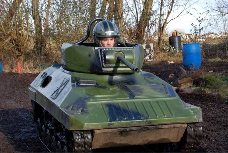 A man driving a Mini Tank across a muddy track