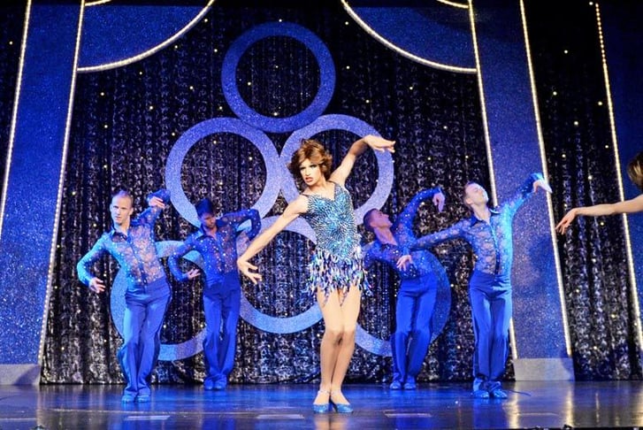 Female and male dancers dressed in glittery blue costumes on a stage