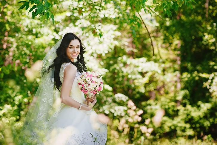 A bride posing for her wedding photos in a forest, holding her bouquet 