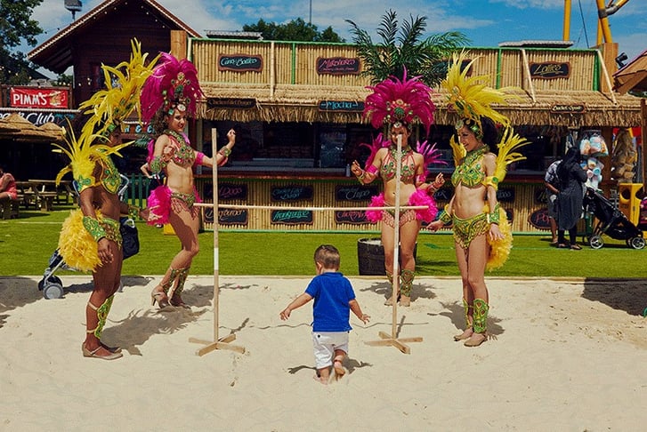 Urban Beach Festival entertainers dressed in carnival clothes playing limbo with a kid
