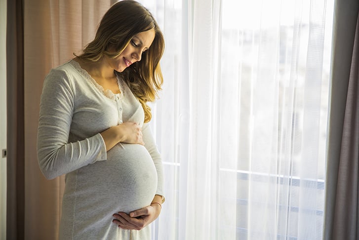 Pregnant woman standing next to window