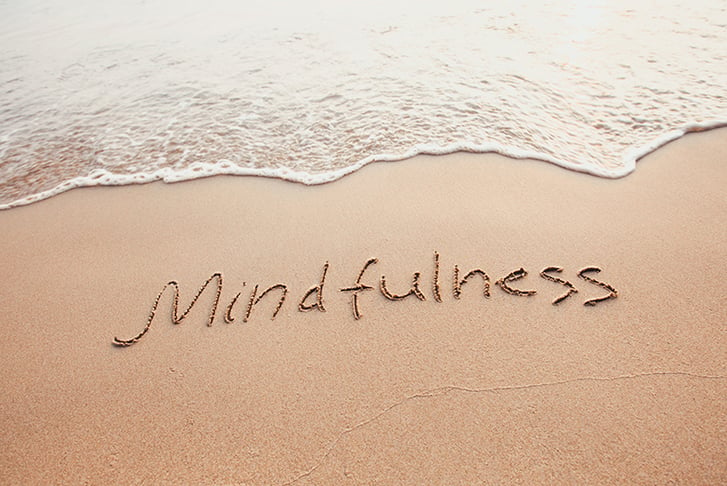 The word 'mindfulness' written in the sand on a beach